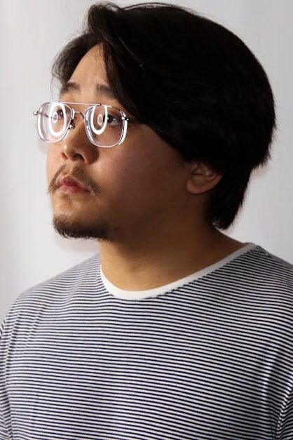 A thoughtful man wearing glasses and a striped shirt, looking to the side in a studio setting.